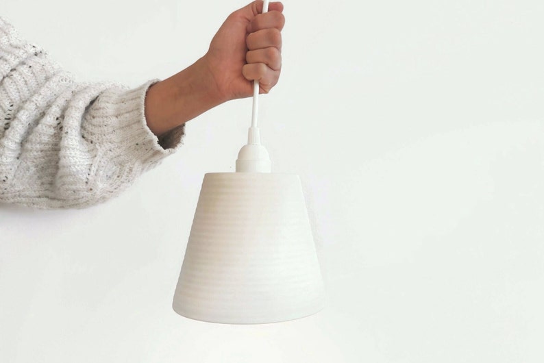 May include: White ceramic pendant light with a ribbed texture. The light is hanging from a white cord.
