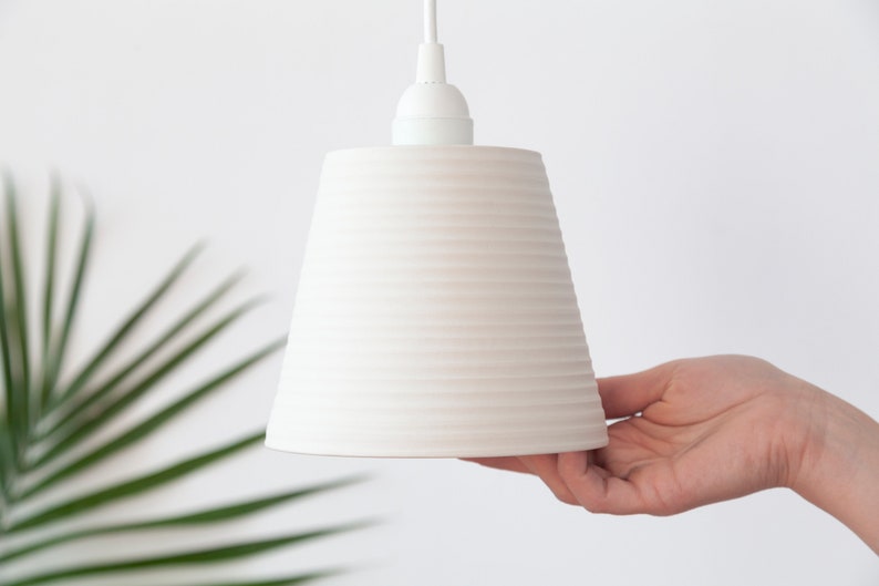 May include: White ceramic pendant light with a ribbed design. The light is hanging from a white cord.