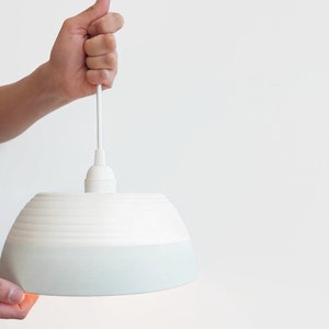 May include: A white ceramic pendant light with a light blue glaze on the bottom half. The light is hanging from a white cord.