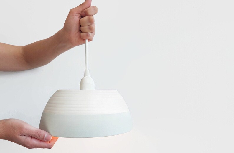 May include: A white ceramic pendant light with a light blue glaze on the bottom half. The light is hanging from a white cord.