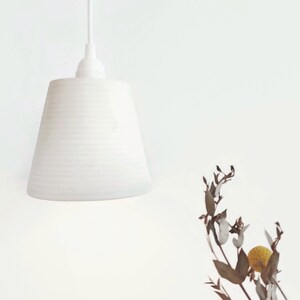 May include: A white ceramic pendant light with a ribbed texture hangs from a white ceiling. The light is off and the background is a white wall.