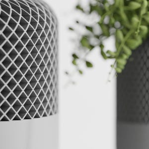 May include: Two white cylindrical planters with a black grid pattern. The planter on the right has a green plant growing out of it.