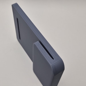 May include: A grey, rectangular object with a slot and a curved base. The object has a textured surface and appears to be made of a solid material. The design is minimalist and modern, suitable for various uses.