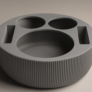 May include: A gray, circular organizer with a ribbed exterior. It features two small round openings, two rectangular slots, and a large central oval space. The design is modern and minimalist.