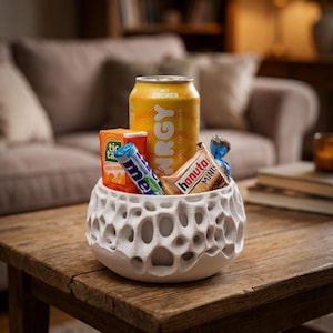 Puede incluir: Un cuenco de cerámica blanca texturizada lleno de snacks y una lata de bebida energética amarilla. El cuenco está sobre una mesa de madera. Otros artículos incluyen Tic Tac, un rollo de Mentos y un paquete de Hanuta Minis.