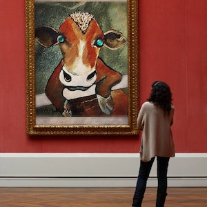 May include: A framed painting of a brown and white cow with blue eyes. The cow is looking directly at the viewer. The painting is in a gold frame and is hanging on a red wall.