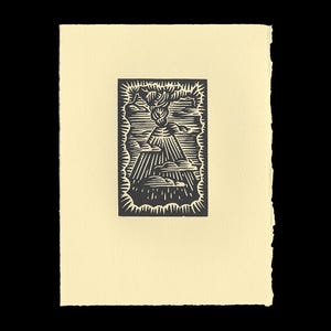 May include: A black and white linocut print depicting a volcano erupting, with clouds and rays of light. The print is on a cream-colored paper with a rough, uneven edge. The artwork is centered on the paper.
