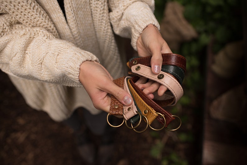 May include: A set of five leather keychains in various colors, including brown, pink, green, and yellow. Each keychain has a metal ring and a decorative stitch detail.