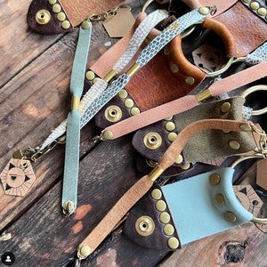 May include: A collection of leather bracelets with metal accents and beads. The bracelets are in various colours, including brown, pink, green, and blue. Some of the bracelets have a braided design.
