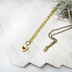 May include: A gold necklace with a teardrop-shaped pendant. The necklace is made of two chains, one thicker than the other. The pendant is smooth and shiny.
