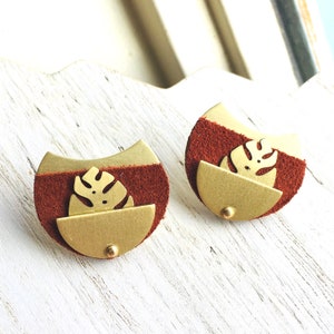 May include: A pair of earrings with a brown suede backing and a gold metal front. The front features a cut-out leaf design.