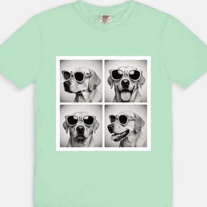May include: A light green t-shirt featuring a square graphic of four black and white images of a dog wearing sunglasses. The dog is a Labrador Retriever. The t-shirt is made of a soft, comfortable material.
