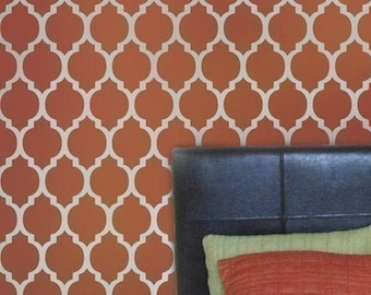 May include: A bedroom with a headboard and pillows. The wall behind the bed is painted a burnt orange color and features a white stencil pattern of a repeating geometric design.
