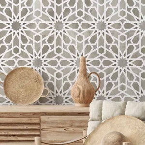 May include: A light grey wallpaper with a white geometric pattern of stars. A wooden chair with a light grey cushion and a straw hat on it. A wooden cabinet with a straw tray and a woven vase on top.