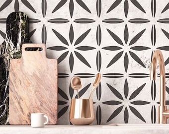 Puede incluir: Una encimera de cocina con un salpicadero de azulejos blancos con un patrón geométrico de formas de flores negras. La encimera tiene una superficie de mármol blanco con un grifo, dos tablas de cortar, una taza y un portautensilios de cobre.