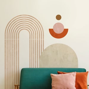 May include: A teal green sofa with wooden legs and two pillows, one pink and one orange, sits in front of a white wall with a brown, pink, and orange geometric design.