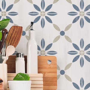 May include: A kitchen countertop with a white background featuring a blue and beige patterned tile design. The countertop has a variety of kitchen items, including a wooden cutting board, a white ceramic bottle, two salt and pepper shakers, a wooden spoon, a wooden spatula, and a white bowl with green lettuce.