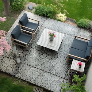 May include: An outdoor patio set comprising two armchairs, a loveseat, and a small side table, all with navy blue cushions and light wood frames. A white slatted coffee table is positioned between the chairs. The patio floor has a black and white circular pattern.