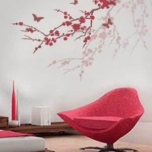 May include: A red chair with a unique design sits in a room with a white wall featuring a stencil of a cherry blossom branch with butterflies.