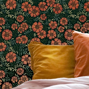 May include: Two orange velvet throw pillows with ruffled edges on a bed with a dark green floral patterned headboard.