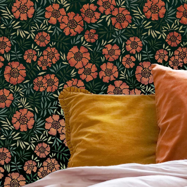 May include: Two orange velvet throw pillows with ruffled edges on a bed with a dark green floral patterned headboard.