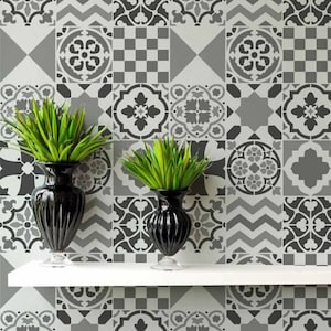 May include: Two black vases with green plants on a white shelf, set against a patterned tile wall. The tiles display geometric and floral designs in grey and white. The vases are approximately 30 cm tall.
