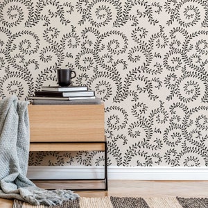 May include: A wooden nightstand with a black metal frame and a stack of books on top. The nightstand is in front of a wall with a beige wallpaper featuring a black floral pattern.