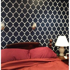 May include: A bedroom with a dark blue wall featuring a white geometric pattern. The bed has a dark wood headboard and a red duvet cover. There are two wall sconces with white glass shades on either side of the bed. A lamp with a white shade is on a nightstand next to the bed.