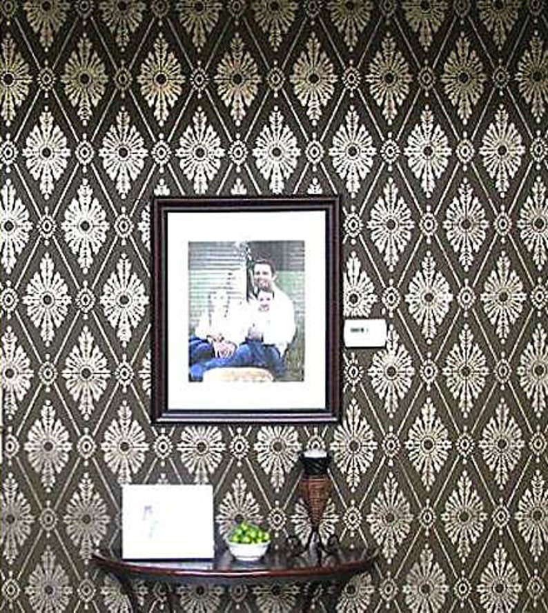 May include: A brown wall with a white geometric pattern. A framed photo of a family of three is hanging on the wall. A small table with a vase and a bowl of limes is in front of the wall.