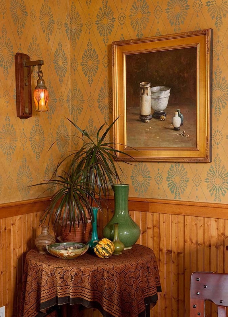 May include: A small table with a brown tablecloth and a green vase with a gourd on top. There are other vases and a bowl on the table. The table is in a room with wood paneling and a patterned wallpaper.