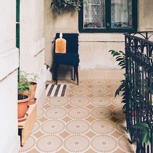May include: A patio with a patterned tile floor. The tiles are beige with a white geometric design. There is a black chair with a wooden cutting board leaning against it. There are potted plants on a wooden shelf.