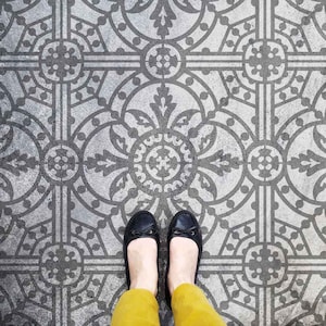 May include: A pair of black shoes with a bow on the front are standing on a grey and white patterned floor.