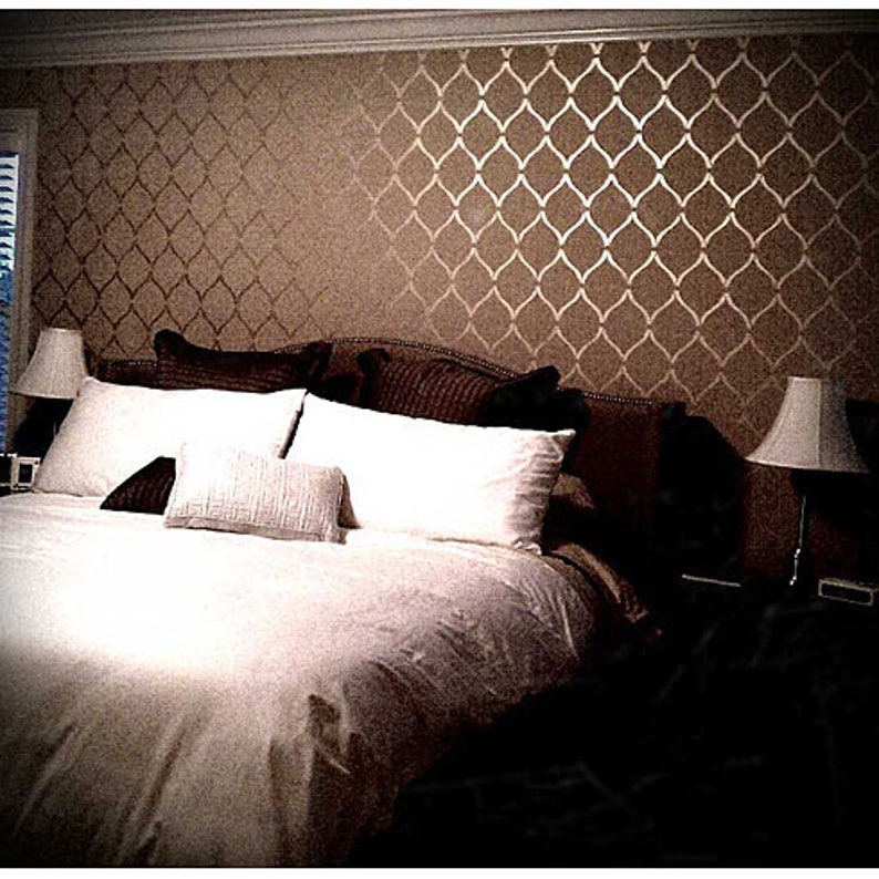 May include: A white bed with a brown headboard and white pillows. The wall behind the bed is painted a light brown color and has a gold stencil pattern.