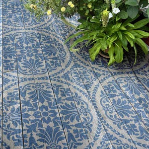 May include: A wooden floor with a blue and white damask pattern painted on it. The floor is made of individual planks of wood. The pattern is a traditional damask design with a repeating motif of leaves and flowers.