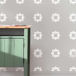 May include: A light grey wall with a white stencil pattern of repeating four-pointed stars. A green cabinet with a wooden top is in the foreground.