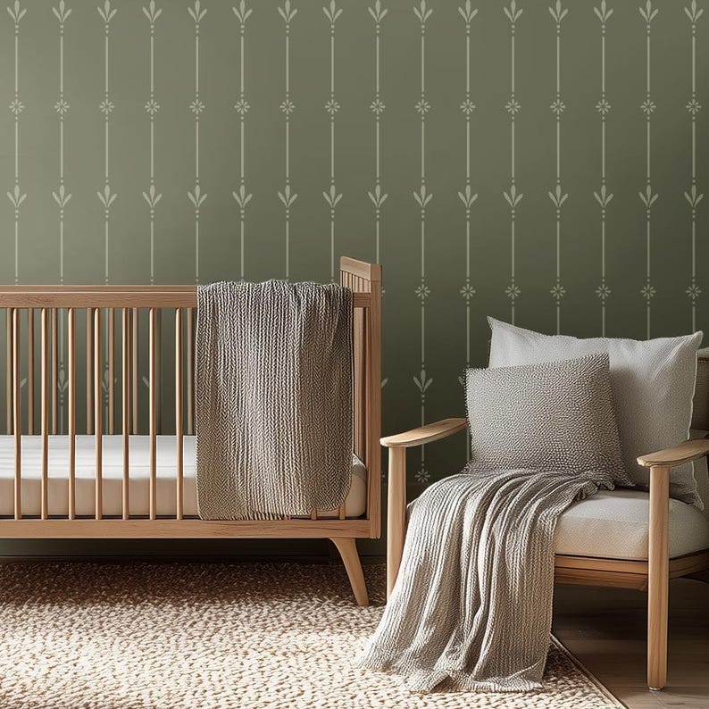 May include: A nursery scene featuring a wooden crib with a gray blanket and a wooden chair with pillows and a blanket. The wall is painted olive green with a white floral pattern.