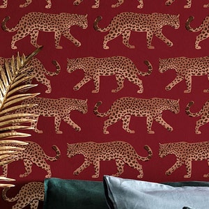 May include: Red wallpaper with a repeating pattern of gold leopard silhouettes. The leopards are walking in a staggered pattern, with their spots and stripes visible.