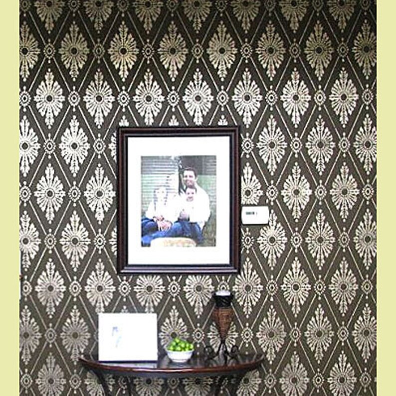 May include: A brown wall with a white diamond pattern stencil design. A framed photo of a family of three is hanging on the wall. A small table with a vase and a bowl of green limes is in front of the wall.