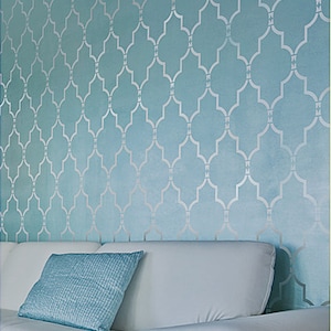 May include: A white couch with a light blue throw pillow in front of a wall with a light blue and silver geometric pattern.