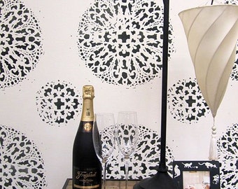 May include: A black and white patterned wall with a black metal floor lamp with a white fabric shade. A bottle of champagne, two wine glasses, and a small framed picture are on a table in front of the wall.
