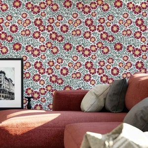 May include: A red couch with pillows in front of a wall with a floral pattern. The pattern features red flowers with yellow centers and green leaves on a white background.