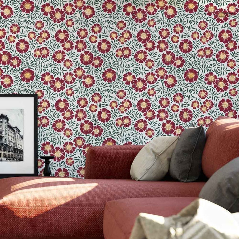 May include: A red couch with pillows in front of a wall with a floral pattern. The pattern features red flowers with yellow centers and green leaves on a white background.