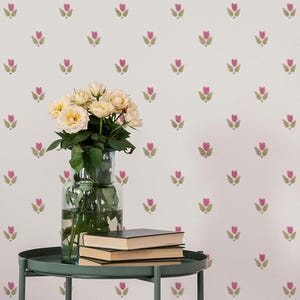 May include: A still life featuring a bouquet of yellow roses in a clear glass vase, set on a dark green metal side table. Two books are stacked on the table. The background is a white wall with a repeating pink and green floral pattern.