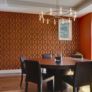 May include: A dining room with a round wooden table and six black leather chairs. The wall is painted orange and features a black geometric stencil pattern. A modern chandelier hangs above the table.