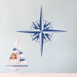 May include: A blue nautical compass stencil on a light blue wall with a small sailboat model in the foreground.