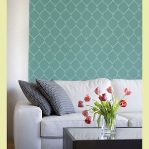 May include: A white couch with two pillows and a vase of pink tulips on a coffee table in front of a teal wall with a geometric pattern.