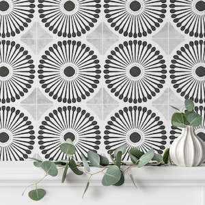 May include: Black and white geometric wallpaper with a repeating pattern of stylised sunbursts. The wallpaper is shown on a white surface with a branch of eucalyptus leaves.