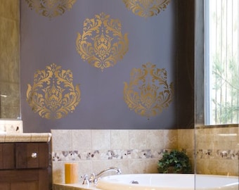 May include: A bathroom with a white bathtub and a gray wall with gold damask stencil designs. The bathroom has a brown cabinet and a tiled floor.
