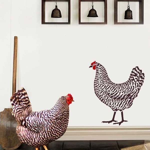May include: Two black and white patterned chicken silhouettes on a white wall. The chickens are facing different directions. The wall has three square wooden frames with black bells hanging inside.