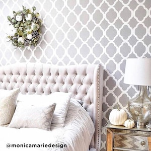 May include: A white and gray patterned wallpaper with a trellis design. A white upholstered headboard with tufted buttons is in front of the wallpaper. A white pumpkin sits on a nightstand with a silver lamp.